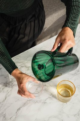 product photography, interior, woman pouring water from a green jug in a glass on marble table 