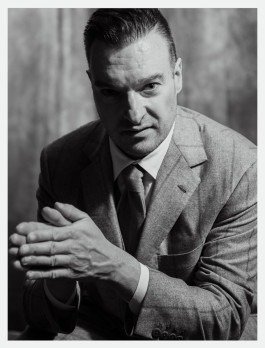 Schwarz-weißes Portrait eines Musikers in klassischer Kleidung, die Hände gegeneinander gelegt. 