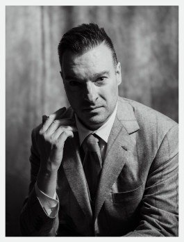 Schwarz-Weiß-Porträt eines Musikers in einem klassischen Anzug mit der Hand neben dem Gesicht. 